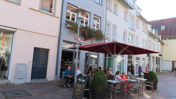 Außenansicht des Liquid Beans Cafés mit Gästen auf der sonnigen Terrasse