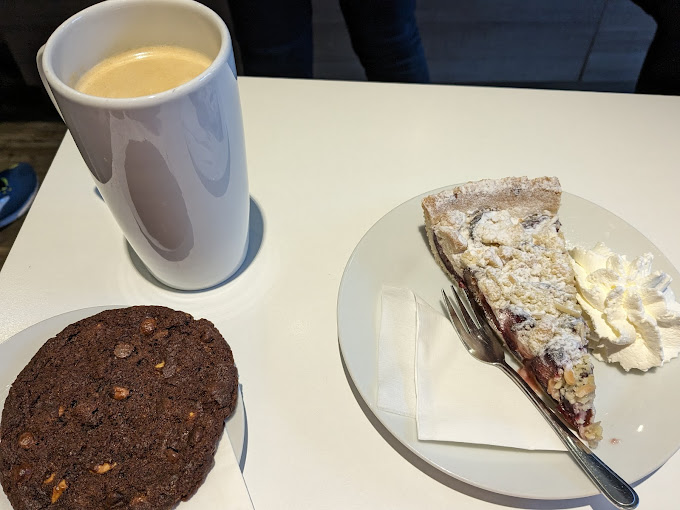 Tasse Cappuccino mit Schokokeks und Stück Kuchen